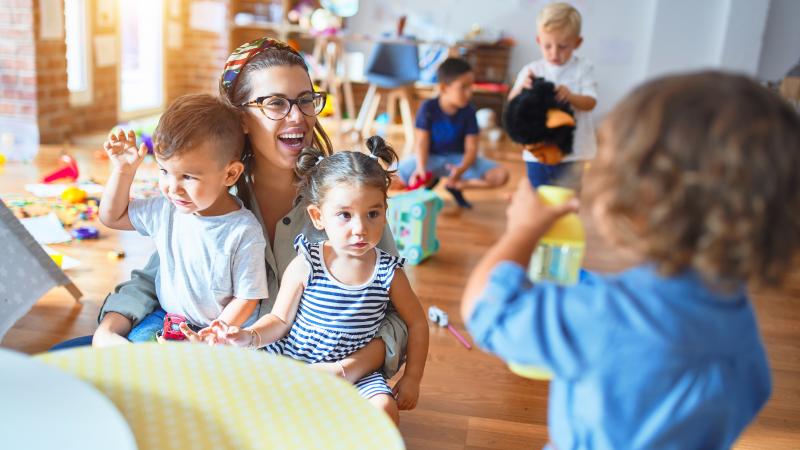 Early intervention. Little girl holds something in her hands. Woman, who has two toddlers on her lap sees what the litte girl is holding