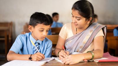 Boy and teacher sitting on a desk. They write in their notebooks 2 